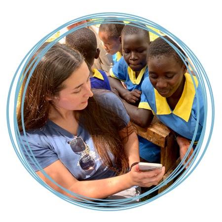 A U N E student studying abroad shows their mobile phone to a group of young children in Kenya